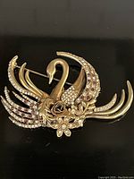 Photo showing the large swan pin decorated with purple and clear stones, with detailed floral accents on gold-tone metal.
