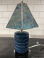 Full lamp showing ceramic ocean blue textured base and stained glass tapered shade with floral wire designs.