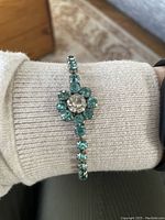 Signed Jayflex sterling silver rhinestone bracelet on wrist, showing central flower design with clear and blue-green stones.