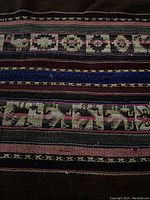 Close up of the textile showing geometric traditional aguayo patterns in pink, beige, blue, and black horizontal stripes on a dark brown background.