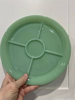 Front view of round, green jadeite glass divided plate with five compartments held in hand.