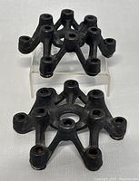 Single cast iron spider-shaped candle holder displayed on clear stand showing detailed side and top angles with 12 candle holes.