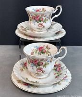 Two Royal Albert vintage teacups displayed stacked on matching saucers and dessert plates, showing the floral pattern and gold trim clearly.