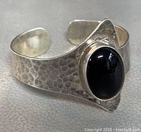 Front three-quarter view showing hammered texture and oval black onyx cabochon.