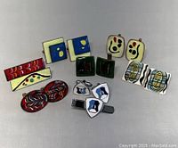 Photo of all MCM cufflinks and tie clips laid out on a light surface showing various abstract enamel designs, colors, and shapes.