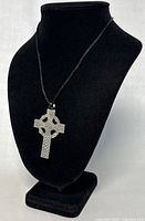 Full view of the Celtic cross pendant on black cord necklace displayed on a black bust stand.