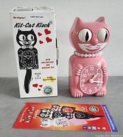 Pink Lady Kit-Cat Klock displayed next to its original box and a product pamphlet showing various Kit-Cat Klock designs.