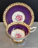 Photo of Royal Stafford teacup and matching saucer showing gold leaf rim, purple band, and pink rose floral center