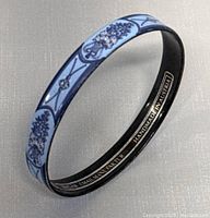 Blue floral enamel bangle bracelet showing overall blue enamel decoration with floral motifs and black interior.