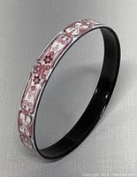Image showing the bangle angled to highlight the floral pink enamel design on a white background and black interior.