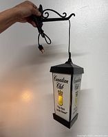 Hand holding vintage Canadian Club hanging wall bar light showing front and side view with cord and mounting hardware.