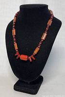 Full front view of the necklace on a black display stand showing the arrangement of wooden and red jasper beads, focusing on the center design.