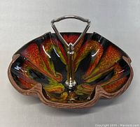 Photo showing leaf-shaped pottery candy dish with vivid red, orange, yellow, and black glaze and a central metal handle.