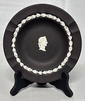 Front view of the vintage Wedgwood black Jasperware plate on stand, showing white classical profile in center and laurel wreath border inside rim.
