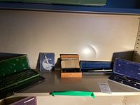 Four separate antique drafting tool cases displayed in a row on a shelf with various compasses and dividers inside.