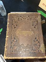 Front cover of the antique photo album showing brown leather with embossed gold decorations and 'Photographs' text