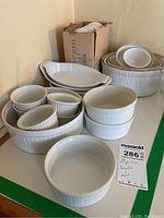 Photo showing a variety of white Apilco ceramic ramekins and casserole dishes of different sizes stacked and grouped on a flat surface. Items have ribbed patterns and some staining.
