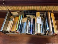 Top-down view of a cardboard box filled with various architecture books, showing the spines and covers of multiple titles.
