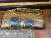 Two area rugs rolled and stacked showing worn edges and backing on top rug.