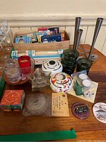Photo showing various candles and candle holders laid out on a table including glass, metal, ceramic holders and boxed candles.