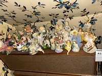 Wide view showing around 30 fairy-themed figurines arranged on a shelf, in various poses and pastel colors
