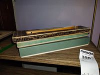 Two boxed handheld folding fans positioned on a wooden table. One fan is fully closed in a brown patterned box, the other in a green box.