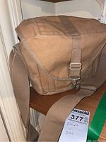 Photo of tan canvas camera bag with adjustable strap and metal buckle, showing exterior condition.