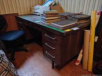 Photo of Joco wood office desk with scratches, showing three drawers on each side and a middle drawer. Desk surface has visible marks and scratches. Chair partially visible beside desk.