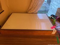 Top view of light box showing the white translucent surface and wooden frame on a table near window.