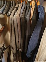 Side view of a row of men's jackets on wooden hangers including a Harris Tweed wool jacket, mostly tweed patterns, in a closet with black shoe trees above.