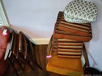 Three wooden mid century modern chair frames stacked, two disassembled, showing spring support seat frames. Cushions in orange and brown stripes and smaller grey patterned cushions stacked on top.