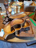 Photo showing assortment of Monkey Pod wooden bowls and trays with salt and pepper sets on a round wooden table.