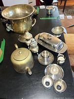 Overall view of lot showing brass champagne bucket, brass kettle, silver plated salt and pepper shakers, several metal egg cups, and butter dish.