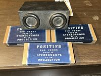 Photo of black stereoscope viewer with two round lenses and three blue and beige cardboard boxes labeled for glass positives for stereoscope and projection.