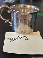 Side view of the sterling silver child's cup showing the engraved design and ornate handle.