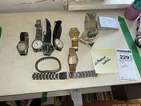 Photo shows seven men's wristwatches arranged on a table, including Timex and Wittnauer brands. Also shows extra metal and chain bracelets.