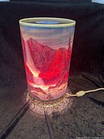 Lamp illuminated showing mountainous waterfall scene on one side in red hues.