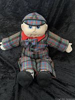 Full view of 1984 Cabbage Patch Doll seated against black fabric background, showing plaid outfit and black felt shoes.