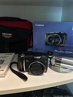 Canon PowerShot SX110 IS digital camera, Tamrac camera bag, mini tripod, user guides, and original box shown together on shelf