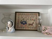 Cross-stitch picture, lamps, devotional bust, and planters on shelf
