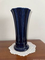 Front view of cobalt blue ceramic fluted vase on white embroidered doily.