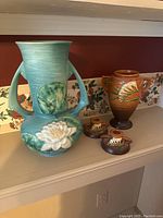 Four vintage Roseville pottery pieces including blue vase with water lily, brown vase with floral design, and two brown candlestick holders