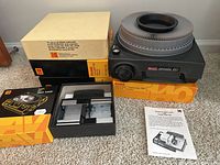 Kodak Carousel 650 projector on carpet surface displayed with four slide trays and original boxes, Kodak EC Stack Loader and instruction manual.