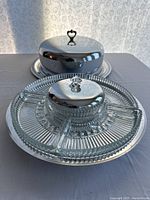 Front view of the two serving pieces including the glass divided tray with center dip bowl and the covered cake plate with cloche and heart-shaped handle knob