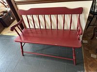 Front angled view of the red farmhouse bench showing the 10 vertical spindles on the backrest, curved arms, and curved top rail.