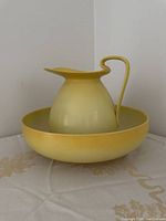 Side view of yellow stoneware pitcher sitting inside the yellow bowl on white fabric background