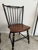 Front angle view showing black spindle back with gold accents and natural wood seat. Solid condition with some marks.