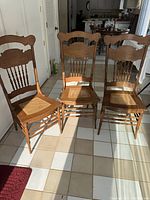 Three antique oak spindle back chairs with caned seats arranged on a tiled floor in sunlight.