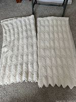 Two off-white hand crocheted afghan blankets laid side by side on a carpeted floor, showing overall pattern and size comparison.