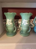 Front view of two green Roseville pottery vases with white flowers and two handles each.